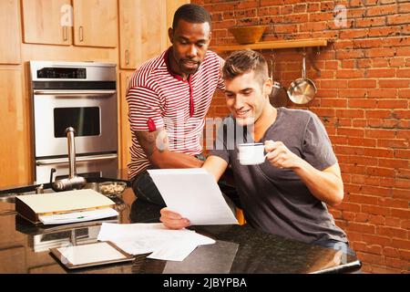 Gay couple looking at paperwork in kitchen Stock Photo