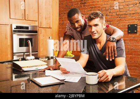 Gay couple looking at paperwork in kitchen Stock Photo