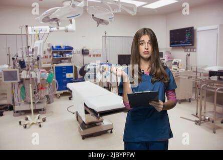 Overworked nurse holding clipboard in hospital room Stock Photo