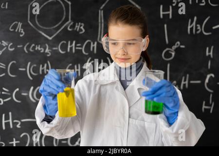 funny scientist child with goggles in lab coat with chemical flasks, blackboard background with science formulas in the laboratory, back to school Stock Photo