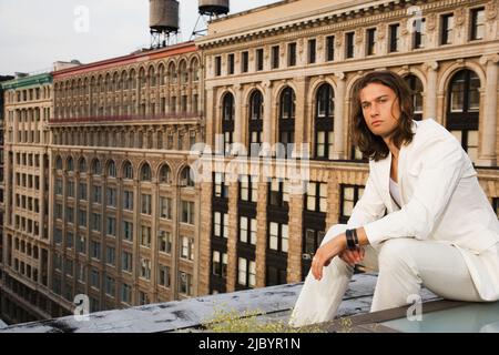 Mixed race man sitting on urban rooftop Stock Photo