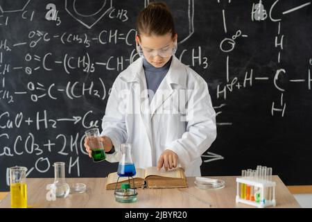young adorable student girl writing a chemistry result on book while doing a scientific experiment and standing in the modern laboratory with Stock Photo