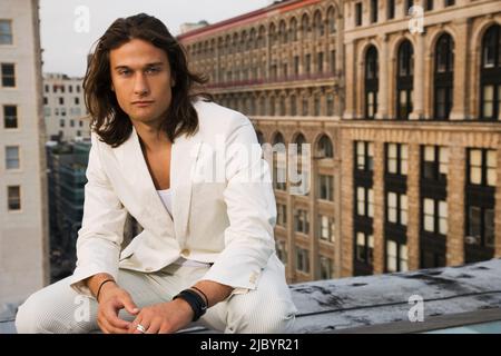 Mixed race man sitting on urban rooftop Stock Photo