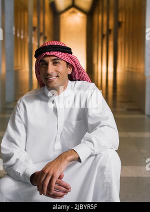 Middle Eastern man in traditional clothing squatting in hallway Stock Photo