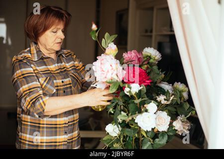 Side view of senior concentrated woman with dark hair spraying bouquet of pink, white roses, setting flowers right. Stock Photo