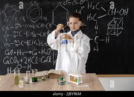 scientist child in lab coat with chemical flasks, blackboard background with science formulas, back to school Stock Photo