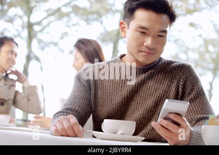 Asian man text messaging on phone in cafe Stock Photo