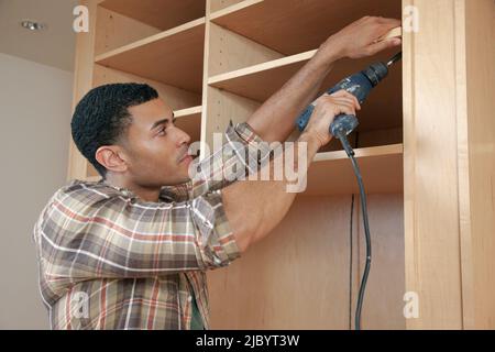 Mixed race man building cabinet Stock Photo
