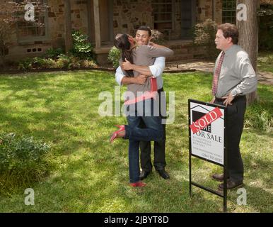 Couple hugging in yard of house with sold sign Stock Photo