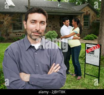 Realtor and couple standing in yard with sold sign Stock Photo