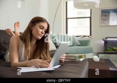 Woman using digital tablet to study on sofa Stock Photo