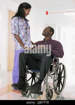 African female nurse looking at patient in wheelchair Stock Photo