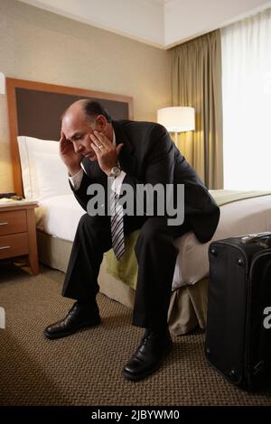 Middle-aged businessman sitting on bed in hotel room Stock Photo