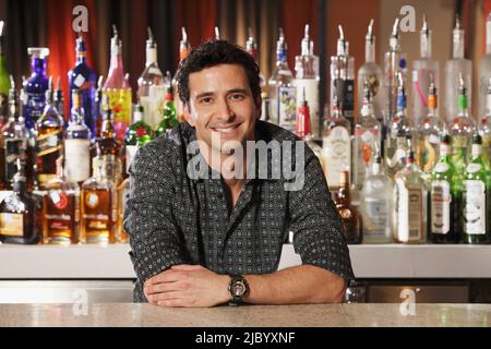 Hispanic male bartender leaning on bar Stock Photo