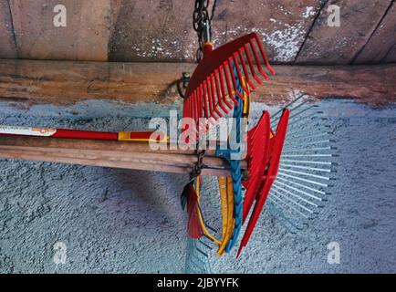 Colorful grass and leaves rakes hanging in the barn Stock Photo