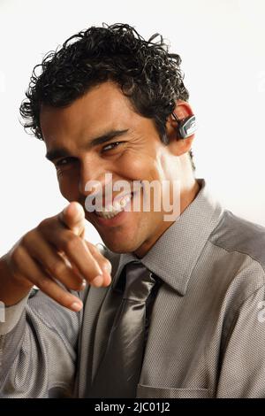 Studio shot of pointing Hispanic businessman with wireless earpiece Stock Photo