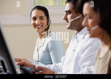 Businesspeople using computers and talking on headsets Stock Photo