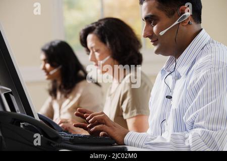 Businesspeople using computers and talking on headsets Stock Photo