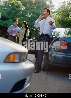 Businessman talking on his cell phone by a car accident Stock Photo
