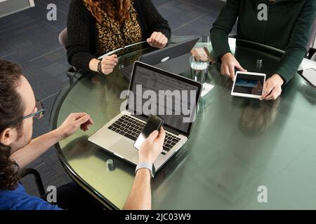 Overhead shot of three people on laptops and tablets during a meeting. Stock Photo