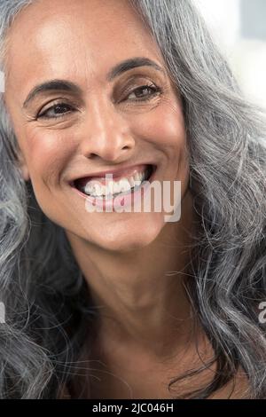 Youthful middle-aged woman with gray hair looks off camera with a big toothy smile Stock Photo