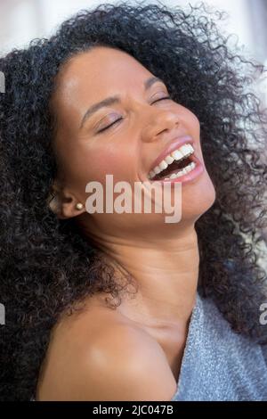 Vertical close up portrait of a mixed race, middle-aged woman laughing with her eyes closed. Stock Photo