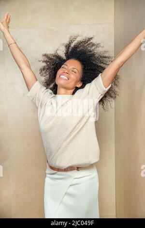 A middle-aged woman with her hands in air and head tilted back laughing. Stock Photo