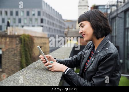 Woman on mobile phone standing at edge of building on rooftop patio Stock Photo