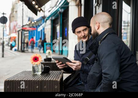 Two men sitting at outdoor cafe table looking at tablet Stock Photo