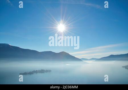 Fog over Brissago Islands on Alpine Lake Maggiore with Sunbeam and Mountain in Ticino, Switzerland. Stock Photo