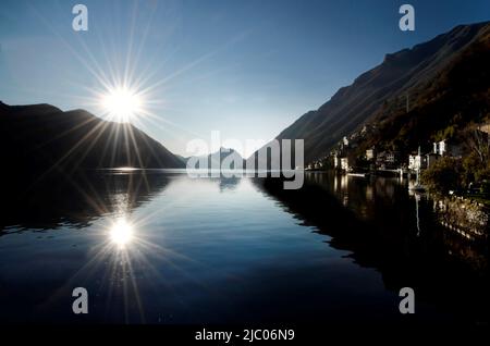 Reflected Sunbeam and Mountain and a Small Village on Lake Como in Lombardy, Italy. Stock Photo