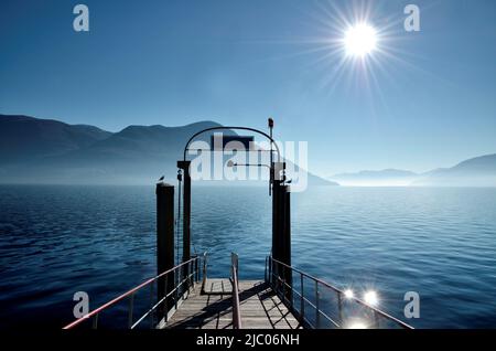 Pier on Alpine Lake Maggiore with Mountain and Sunbeam in Ascona, Switzerland. Stock Photo