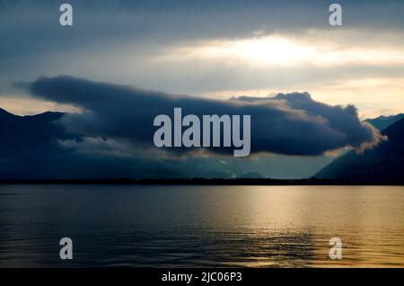 Lonely Cloud Flying over Alpine Lake Maggiore with Mountain in Ticino, Switzerland. Stock Photo