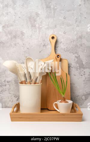 Cooking utensil set on kitchen table aga. Silicone kitchen tools, wooden cutting boards on a tray. Front view. Stock Photo