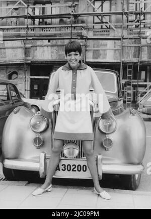 Mary Quant. Born 11 February 1930. British fashion designer and fashion icon. She became an instrumental figure in the 1960s London-based Mod and youth fashion movements.  She was one of the designers who took credit for the miniskirt and hotpants. Picture of her in front of the luxury car wearing a creation of her own with long wide sleaves and a length of the dress well above her knees. 1966 Stock Photo