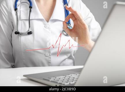 Doctor reporting electrocardiogram results to patient online using laptop. Telemedicine, telehealth concept. Woman in lab coat showing no heart problems with ok hand gesture via videocall. photo Stock Photo