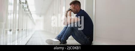 Upset man sitting on floor in hallway Stock Photo