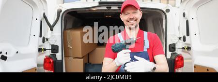 Smiling worker hold screwdriver device in hand in front of truck full of boxes Stock Photo