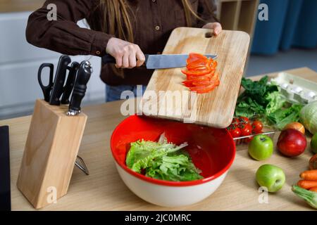 Girl in kitchen preparing fresh salad slicing vegetables throwing red paprika into bowl Stock Photo
