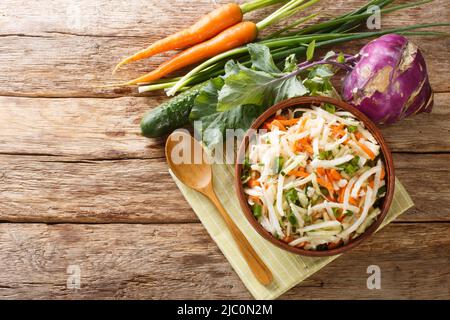 Vegetarian vegetable salad of kohlrabi, carrots, cucumbers and green onions seasoned with oil close-up in a plate on a wooden table. Horizontal top vi Stock Photo
