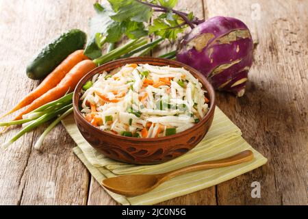 Raw salad of kohlrabi, carrots, cucumbers and green onions seasoned with oil close-up in a plate on a wooden table. Horizontal Stock Photo