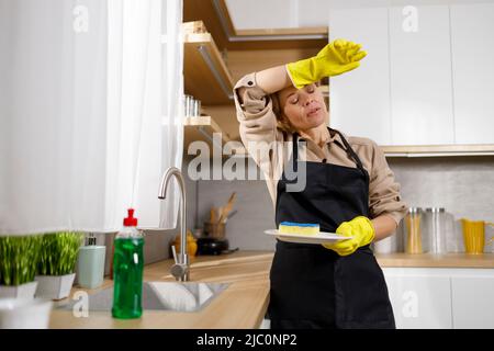 Tired of household chores woman washes dishes in the kitchen Stock Photo