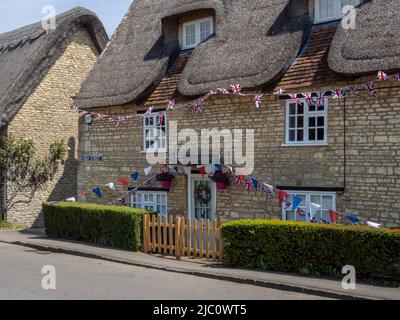 Stone built traditional thatched cottage in the village of Stoke Goldington, Buckinghamshire, UK; decorated with bunting for the Platinum Jubilee Stock Photo