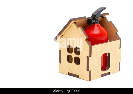 Small red fire extinguisher placed inside a toy wooden house isolated on white background. Home fire safety and prevention measures. Stock Photo