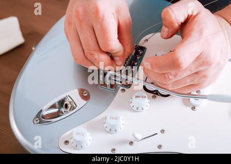 Guitar master making professional guitar maintenance, hands with tools close up. Guitar technician repairing and restringing guitar, top view Stock Photo