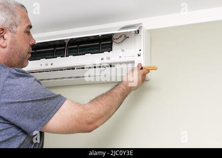 man using screwdriver to repairing air conditioner indoors Stock Photo