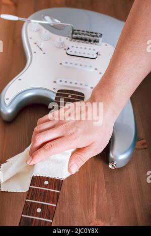 Guitar master polishing fretboard of electric guitar, close up shot of hands with cloth Stock Photo