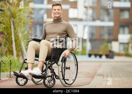 Portrait of cheerful excited handsome young handicapped man sitting in wheelchair outdoors Stock Photo
