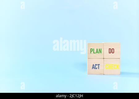 PDCA or Plan Do Check Act cycle method concept. Hand putting action wooden blocks in blue background with copy space. Stock Photo