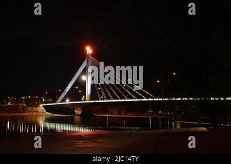 The moon rises behind the "Lumberjack's Candle Bridge" in Rovaniemi, Lapland, Finland, passing over the half frozen Kemijoki river. Stock Photo